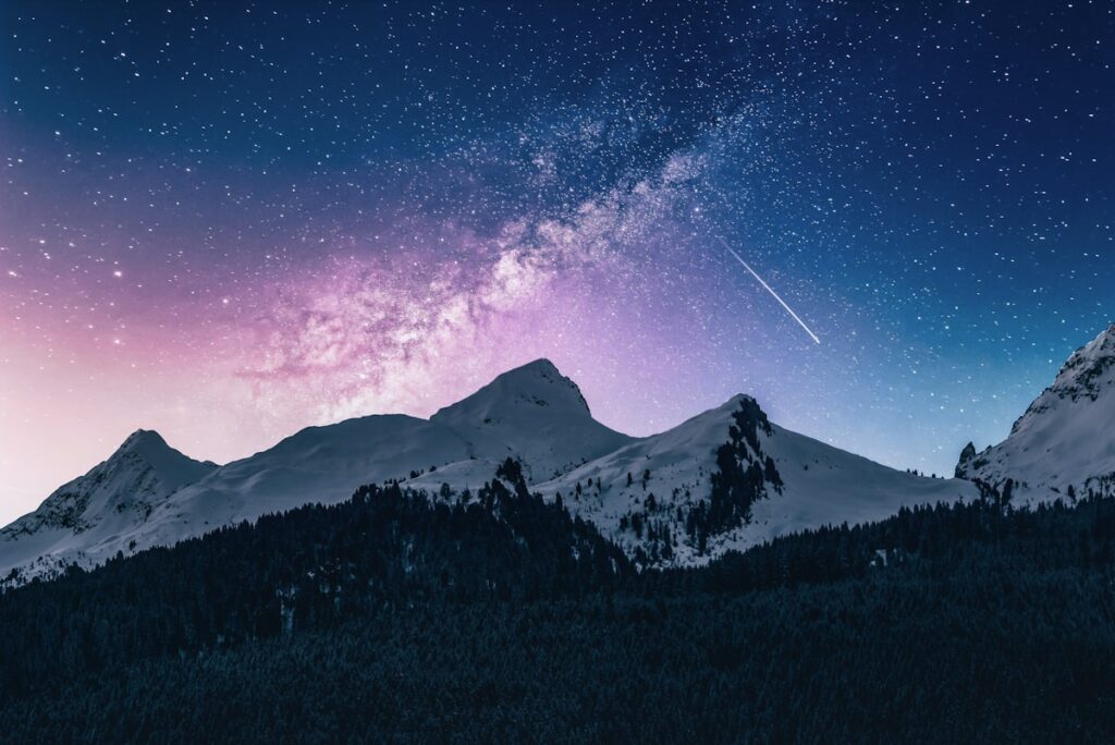 Snow-lit mountain peaks under a starry night sky