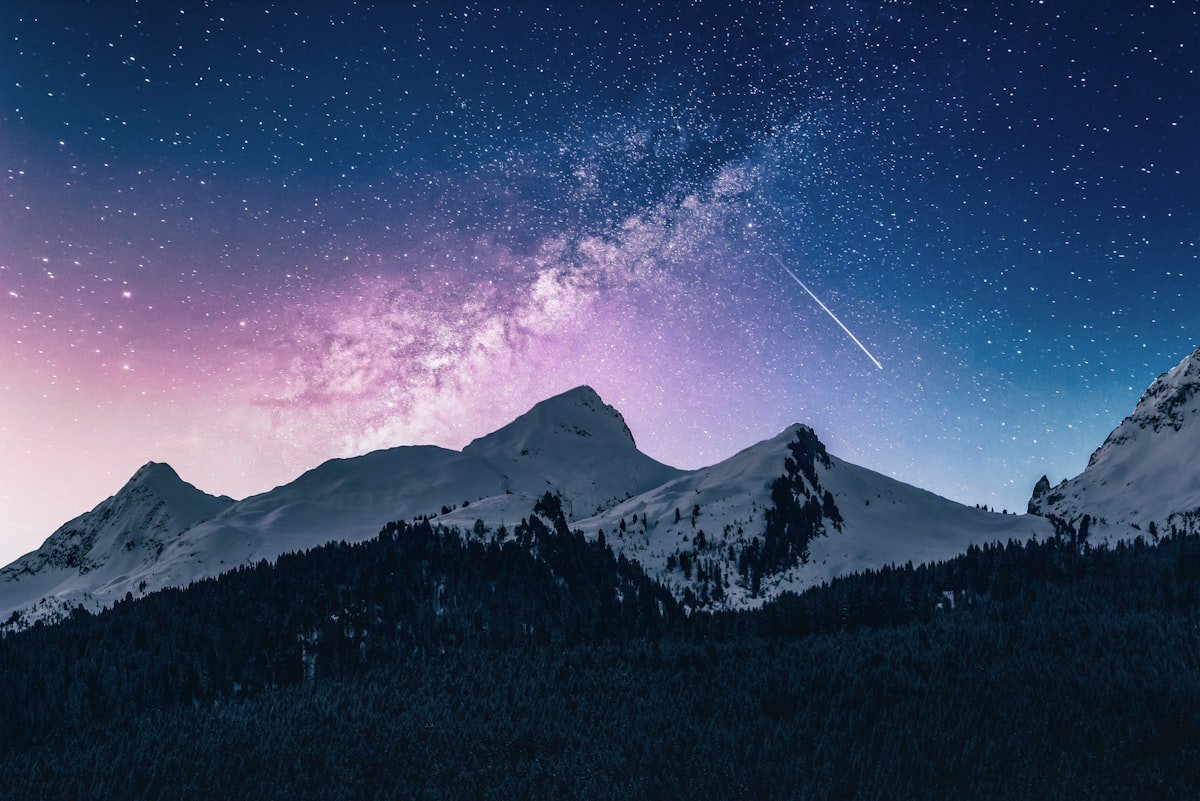 Snow-lit mountain peaks under a starry night sky